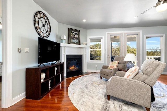 living area featuring a fireplace with flush hearth, baseboards, and wood finished floors