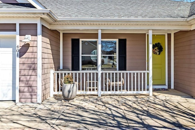 entrance to property with a garage, covered porch, and roof with shingles