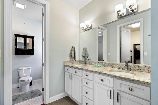 bathroom featuring double vanity, toilet, baseboards, and a sink