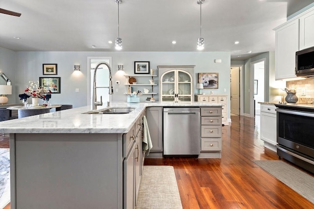 kitchen with backsplash, gray cabinets, dark wood-style floors, stainless steel appliances, and a sink