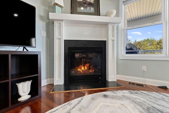 room details with visible vents, baseboards, a fireplace with flush hearth, and wood finished floors