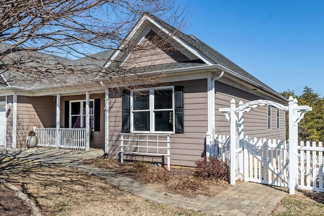 view of front of property with a gate, fence, covered porch, and roof with shingles