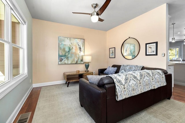 living area featuring visible vents, wood finished floors, baseboards, and ceiling fan