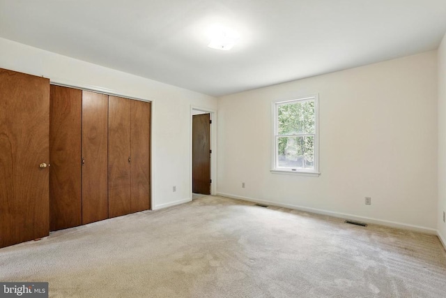 unfurnished bedroom with a closet, light carpet, and baseboards