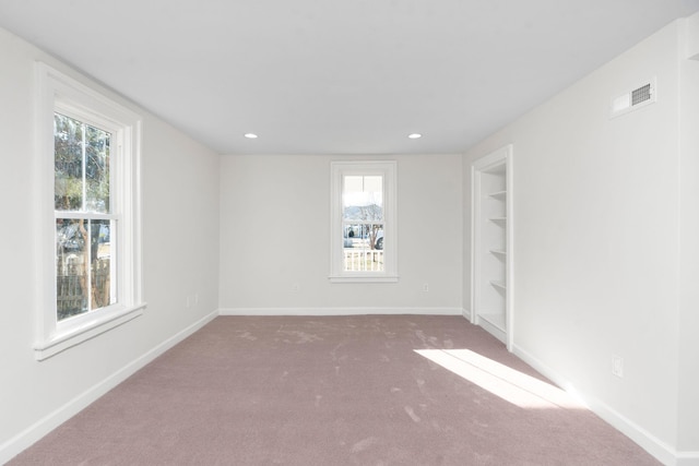 spare room featuring built in shelves, plenty of natural light, and carpet floors