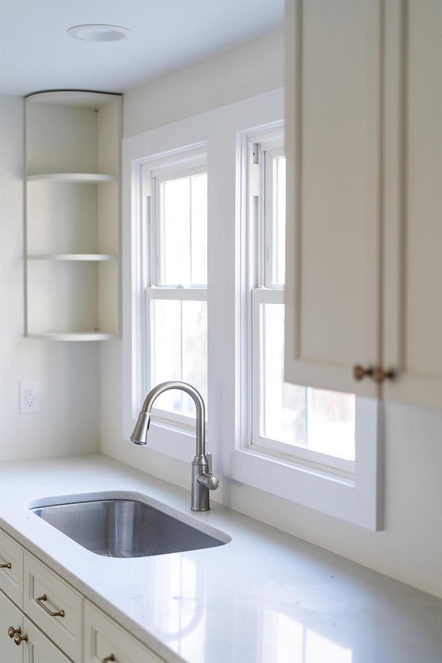 kitchen featuring white cabinetry, light stone countertops, and sink