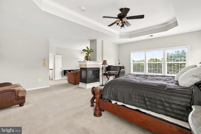  - bedroom with a raised ceiling, ornamental molding, light carpet, a multi sided fireplace, and a ceiling fan
