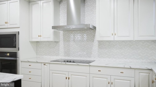 - kitchen featuring wall chimney range hood, oven, built in microwave, white cabinetry, and tasteful backsplash