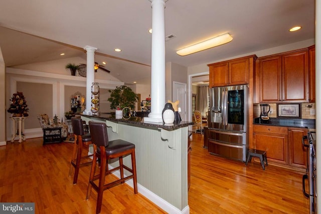 kitchen with a breakfast bar area, brown cabinetry, light wood finished floors, decorative columns, and stainless steel appliances