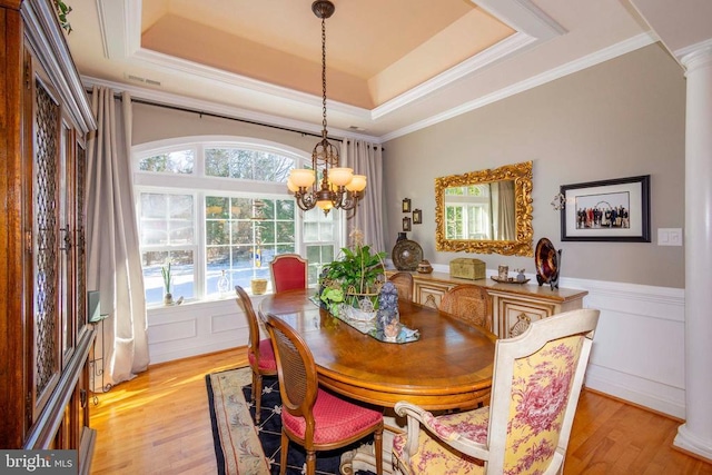 dining space featuring a tray ceiling, light wood finished floors, decorative columns, a chandelier, and crown molding
