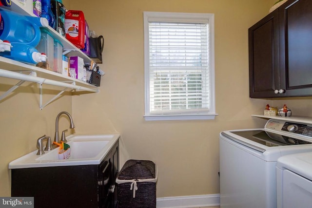 washroom featuring washing machine and clothes dryer, a sink, cabinet space, and baseboards