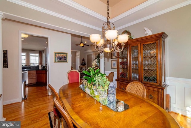 dining room with wainscoting, crown molding, ceiling fan with notable chandelier, and light wood-type flooring