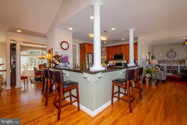 kitchen with brown cabinetry, decorative columns, appliances with stainless steel finishes, recessed lighting, and light wood-style floors