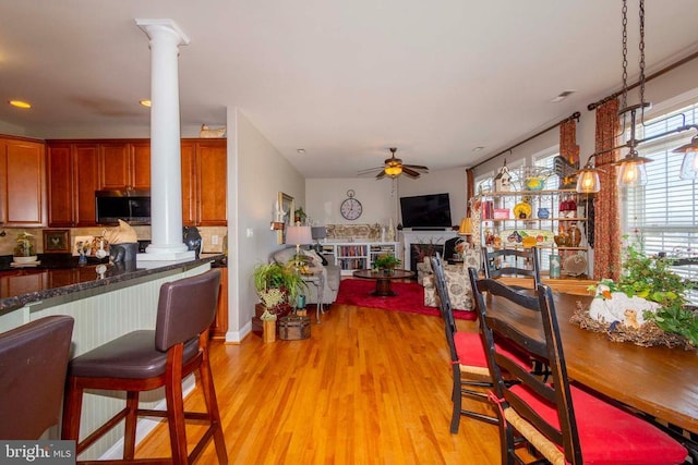 dining area with light wood-style floors, ceiling fan, a fireplace, and decorative columns