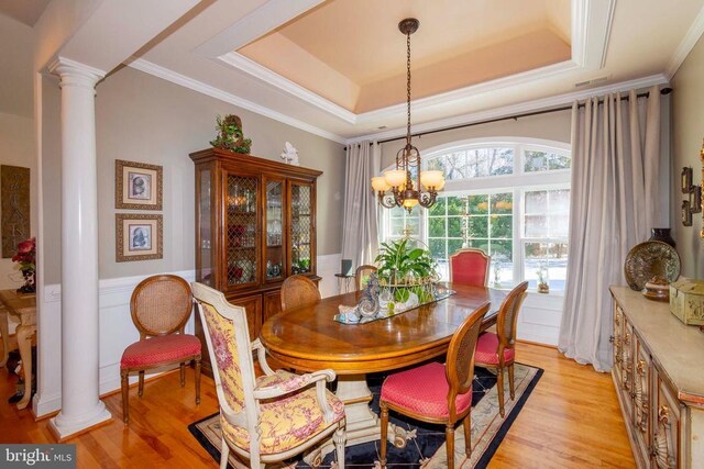 dining room featuring wainscoting, decorative columns, a chandelier, a raised ceiling, and light wood-type flooring