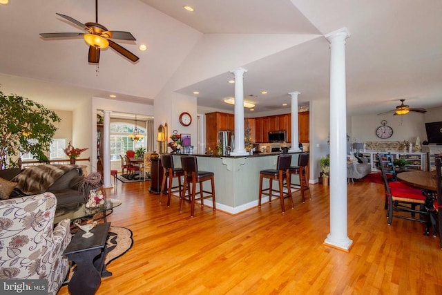 living area with lofted ceiling, a ceiling fan, ornate columns, and light wood-style flooring