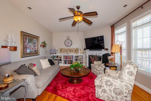 living area featuring ceiling fan, a fireplace, visible vents, and wood finished floors