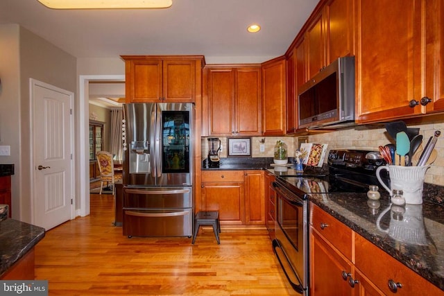 kitchen with dark stone counters, backsplash, appliances with stainless steel finishes, and light wood-type flooring