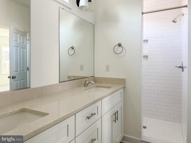 full bathroom with tiled shower, a sink, and double vanity