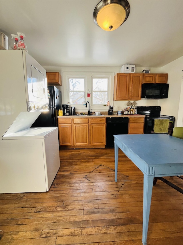 kitchen with stacked washer and dryer, a sink, light countertops, black appliances, and dark wood-style floors