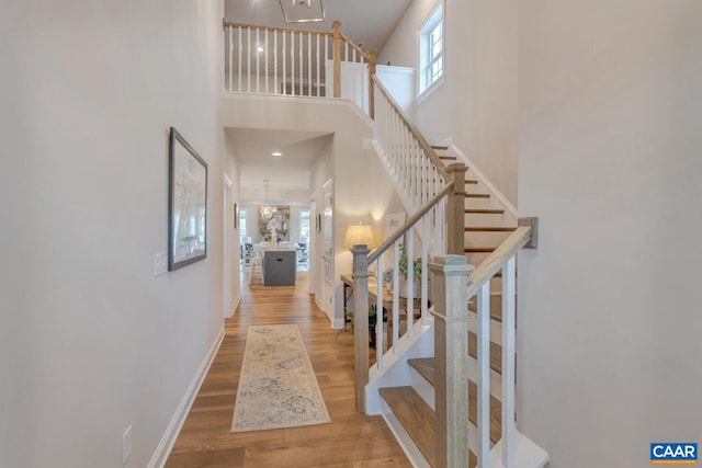 foyer entrance with an inviting chandelier, wood finished floors, baseboards, a towering ceiling, and stairs