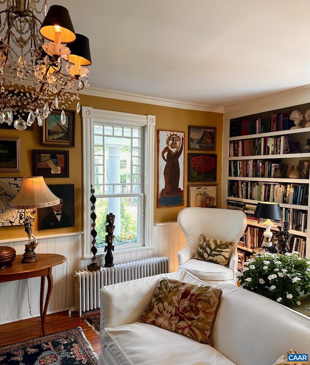 sitting room with wood finished floors, radiator, a wainscoted wall, a notable chandelier, and crown molding