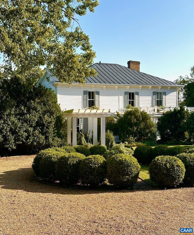view of front facade with metal roof, a standing seam roof, a pergola, and a chimney