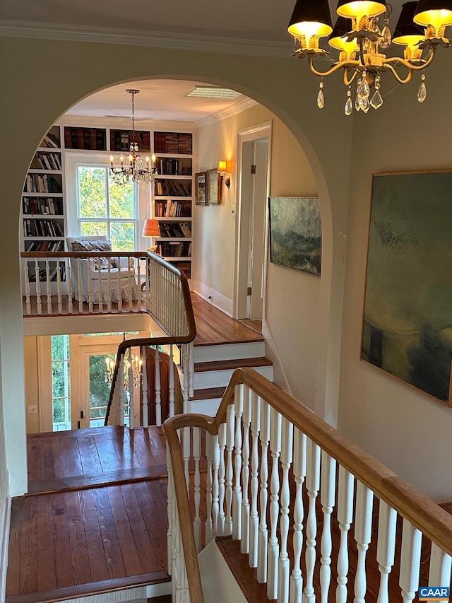 stairway featuring an inviting chandelier, built in shelves, ornamental molding, arched walkways, and plenty of natural light