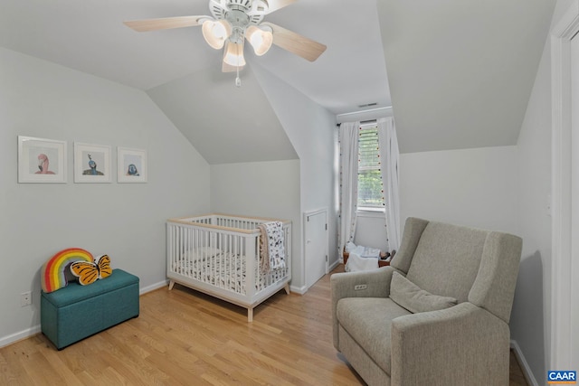 bedroom with wood finished floors, lofted ceiling, a nursery area, baseboards, and ceiling fan