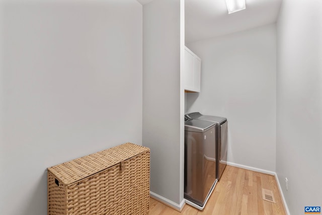 washroom featuring cabinet space, light wood-style flooring, washing machine and dryer, and baseboards