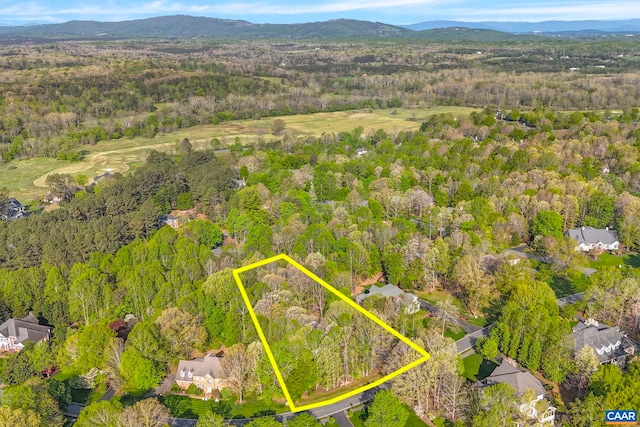 view of property location with a heavily wooded area, property parcel outlined, mountains, and a golf course