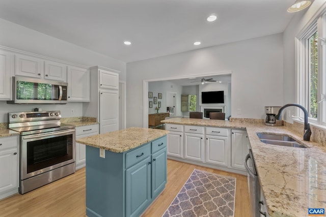 kitchen with appliances with stainless steel finishes, a sink, white cabinetry, light wood-style flooring, and ceiling fan