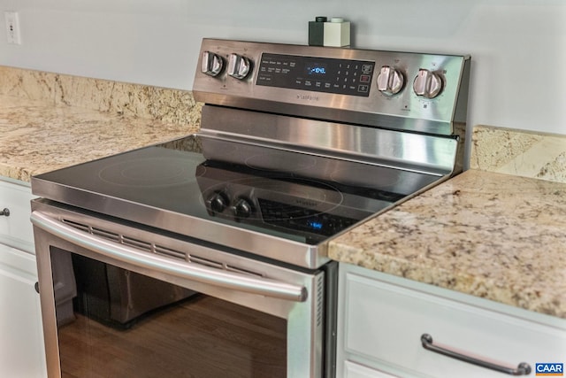 kitchen view of stainless steel range with electric stovetop, white cabinetry, and light stone countertops