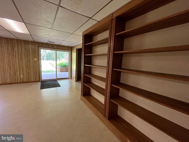  - corridor featuring a paneled ceiling, wooden walls, and baseboards