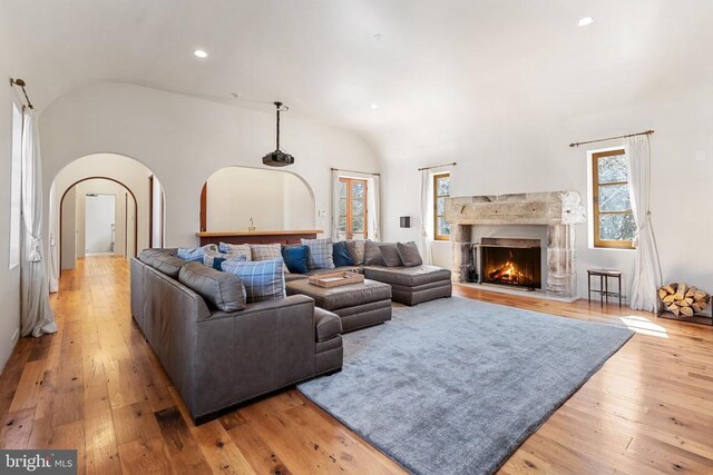  - living area with vaulted ceiling, arched walkways, light wood-type flooring, a fireplace, and recessed lighting
