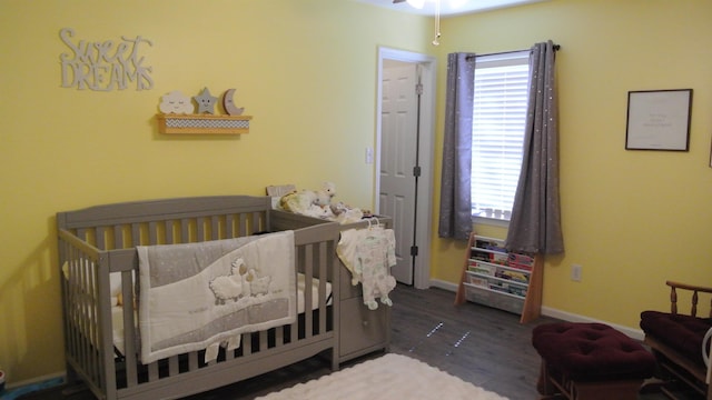 bedroom featuring a nursery area, baseboards, and wood finished floors