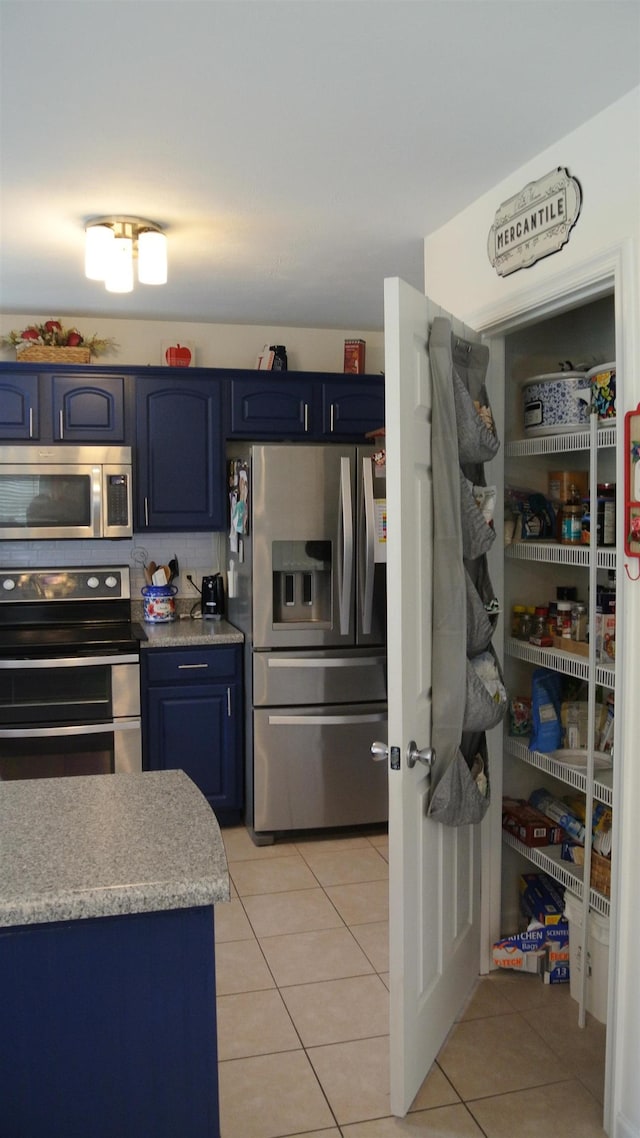 kitchen with light tile patterned floors, light countertops, appliances with stainless steel finishes, and blue cabinets