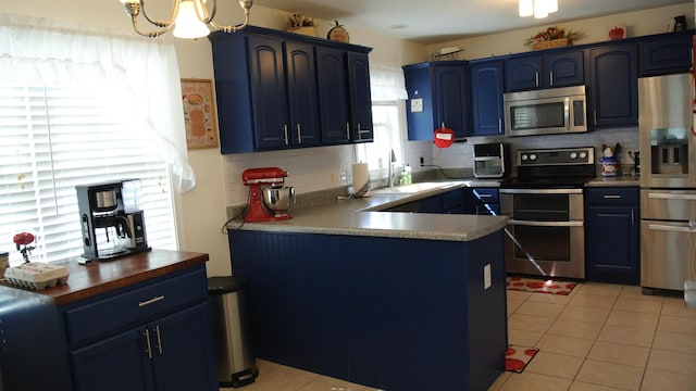 kitchen with light tile patterned floors, decorative backsplash, appliances with stainless steel finishes, a sink, and blue cabinets