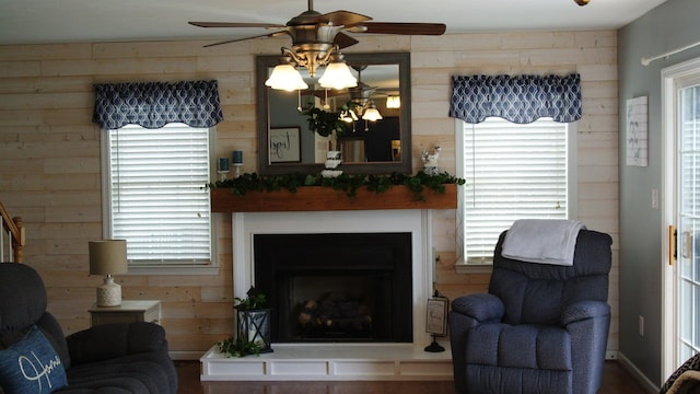 sitting room featuring wood walls, a fireplace with raised hearth, and a ceiling fan