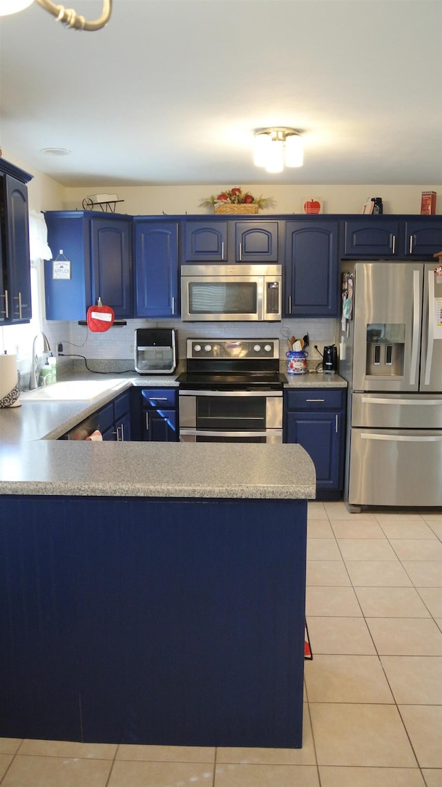 kitchen featuring light tile patterned floors, a peninsula, stainless steel appliances, blue cabinetry, and a sink