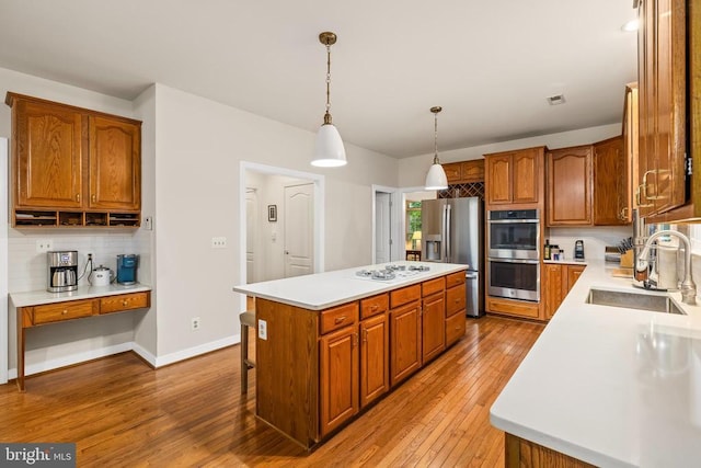 kitchen with a sink, appliances with stainless steel finishes, a center island, light wood finished floors, and light countertops