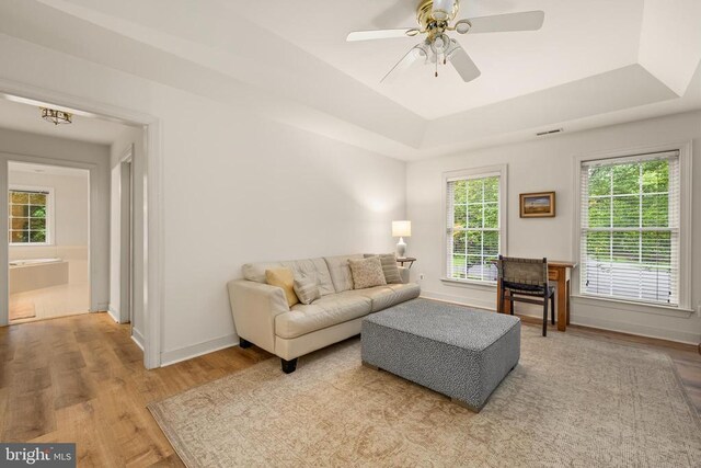 living area featuring a tray ceiling, wood finished floors, ceiling fan, and baseboards
