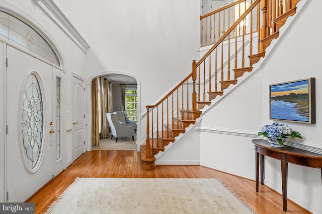 entrance foyer featuring wood finished floors, arched walkways, stairway, a towering ceiling, and baseboards