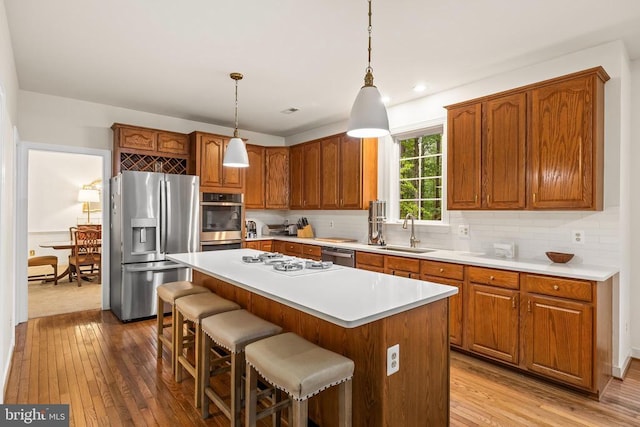 kitchen featuring appliances with stainless steel finishes, a sink, hardwood / wood-style flooring, brown cabinetry, and recessed lighting