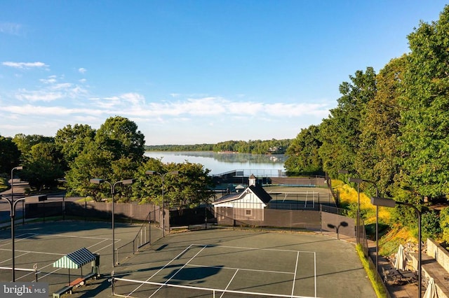 view of tennis court featuring a water view and fence