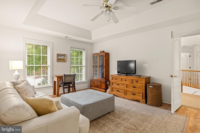 living room featuring light wood-style flooring, ceiling fan, a raised ceiling, and baseboards