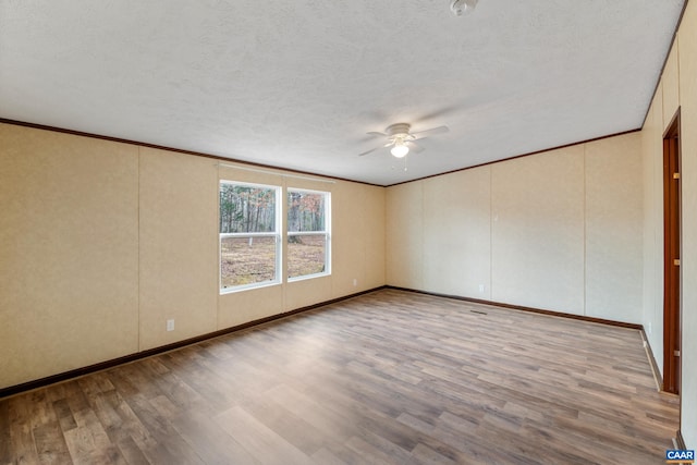 spare room with wood finished floors, a ceiling fan, a textured ceiling, baseboards, and ornamental molding