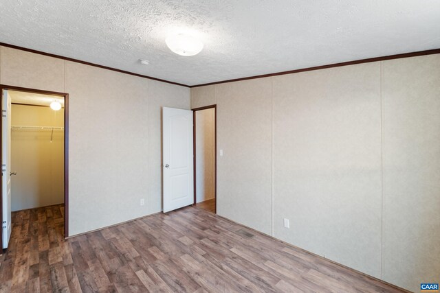 unfurnished bedroom featuring a closet, a textured ceiling, crown molding, a walk in closet, and wood finished floors