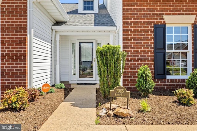 doorway to property featuring brick siding and a shingled roof
