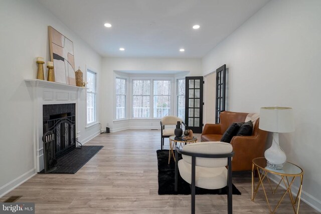 living area featuring baseboards, light wood finished floors, a fireplace with flush hearth, and recessed lighting